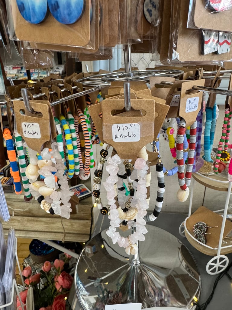 Craft display stand with cardboard tags showing beaded and wrapped items including colorful strings, white stones, and floral decorations on wooden shelving