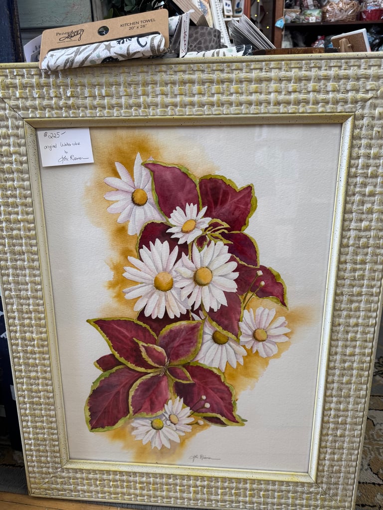 Framed artwork featuring white daisies with yellow centers and dark red foliage on cream background with textured frame.