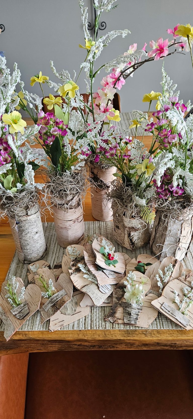 Rustic birch vases with colorful yellow, pink, and white flowers and frosty foliage arranged on a wooden tray display.
