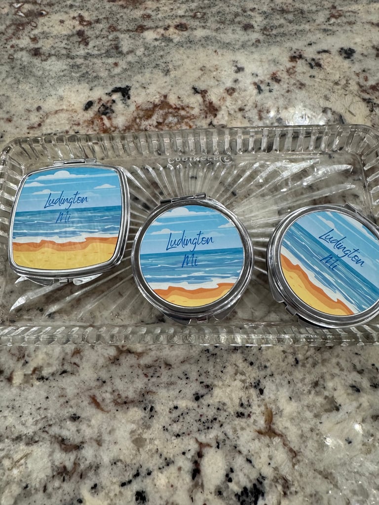 Three lip balm containers with ocean and sandy beach illustrations in a clear plastic tray on granite countertop