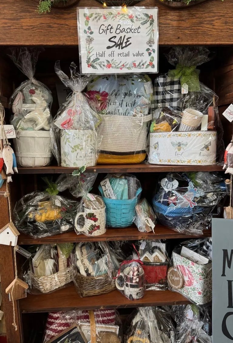 Wooden shelving unit displaying multiple gift baskets wrapped in cellophane, with a sign reading Gift Basket Sale Half off retail value