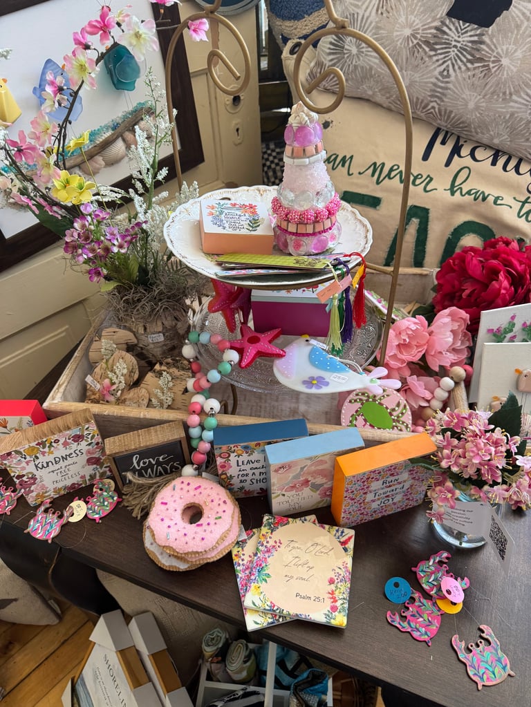 Desk decorated with pink and floral themed items including flowers, decorated cake, donut, cards, and handwritten notes displaying spring and birthday decorations
