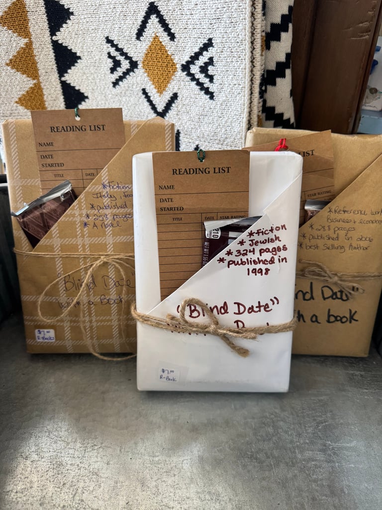 Three kraft paper book bags with reading list labels, tied with twine, containing books and reading materials displayed on concrete surface