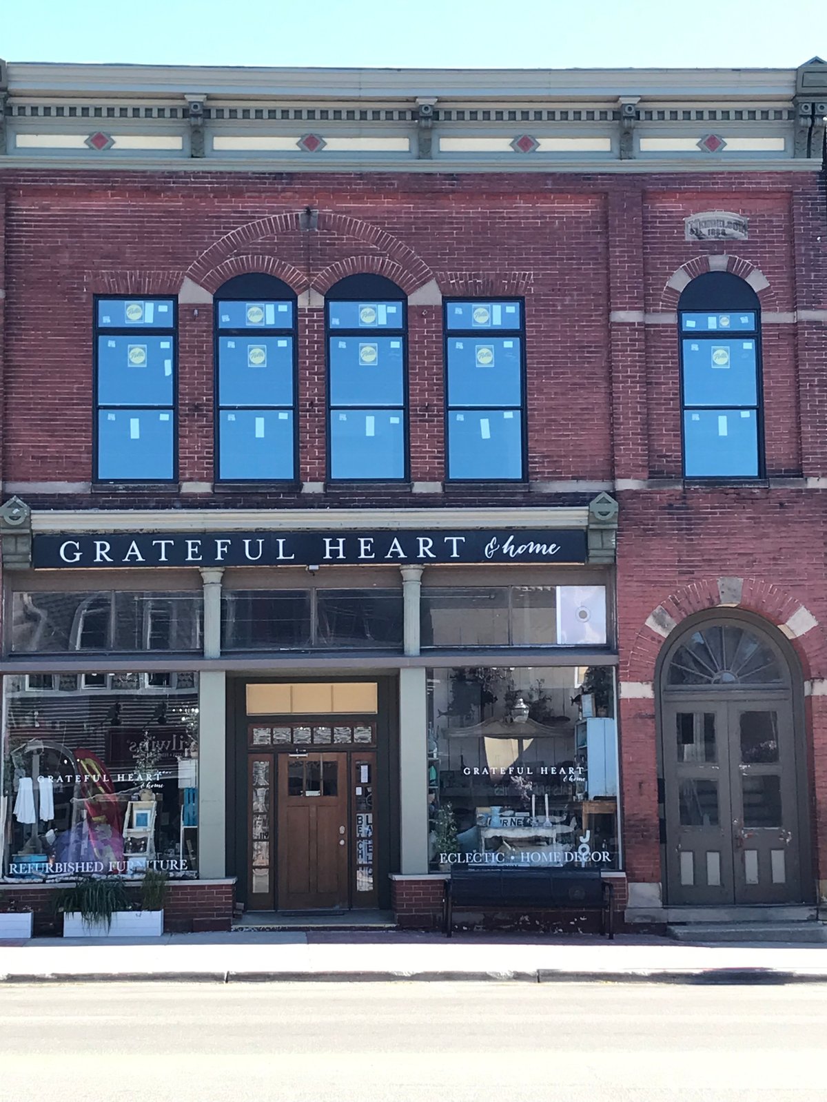 Storefront of Grateful Heart Home shop in a red brick building with blue-trimmed upper windows and dark entrance