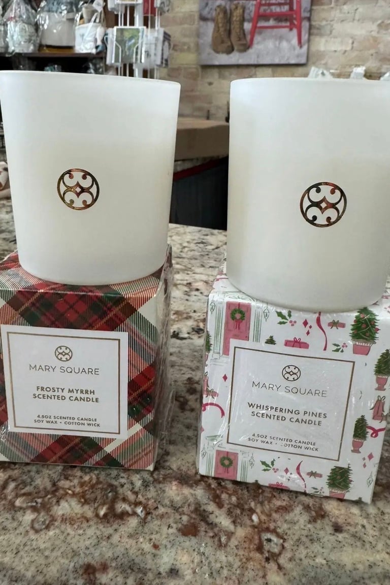 Mary Square scented candles with circular logos displayed on a granite counter, featuring Frosty Myrrh and Glistening Pines fragrances