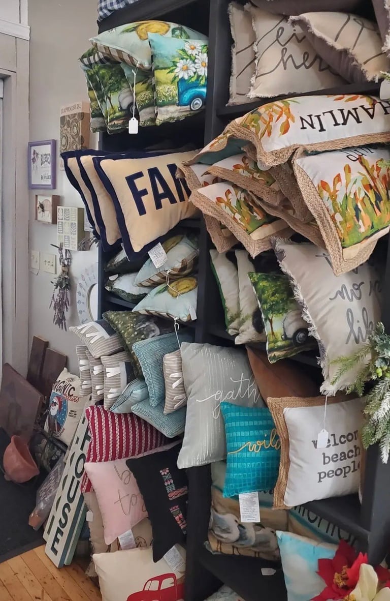 Overflowing shelving unit displaying stacked pillows, cushions, and fabric items with nature and text-based designs in various colors